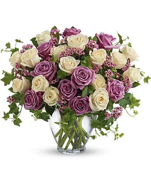 Bouquet of purple and white roses in a clear glass vase on a white background